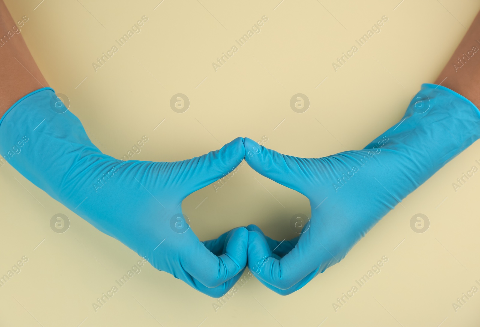 Photo of Person in medical gloves making heart with hands on beige background, top view