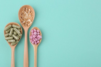 Different vitamin pills in wooden spoons on turquoise background, flat lay. Space for text