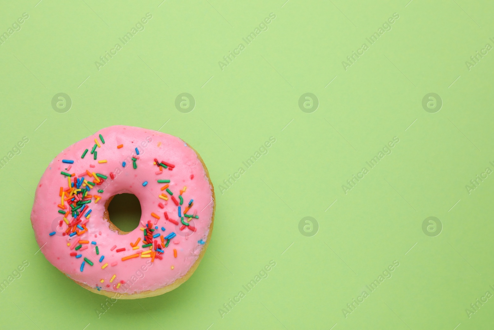 Photo of Tasty glazed donut decorated with sprinkles on green background, top view. Space for text