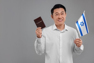 Photo of Immigration. Happy man with passport and flag of Israel on grey background, space for text