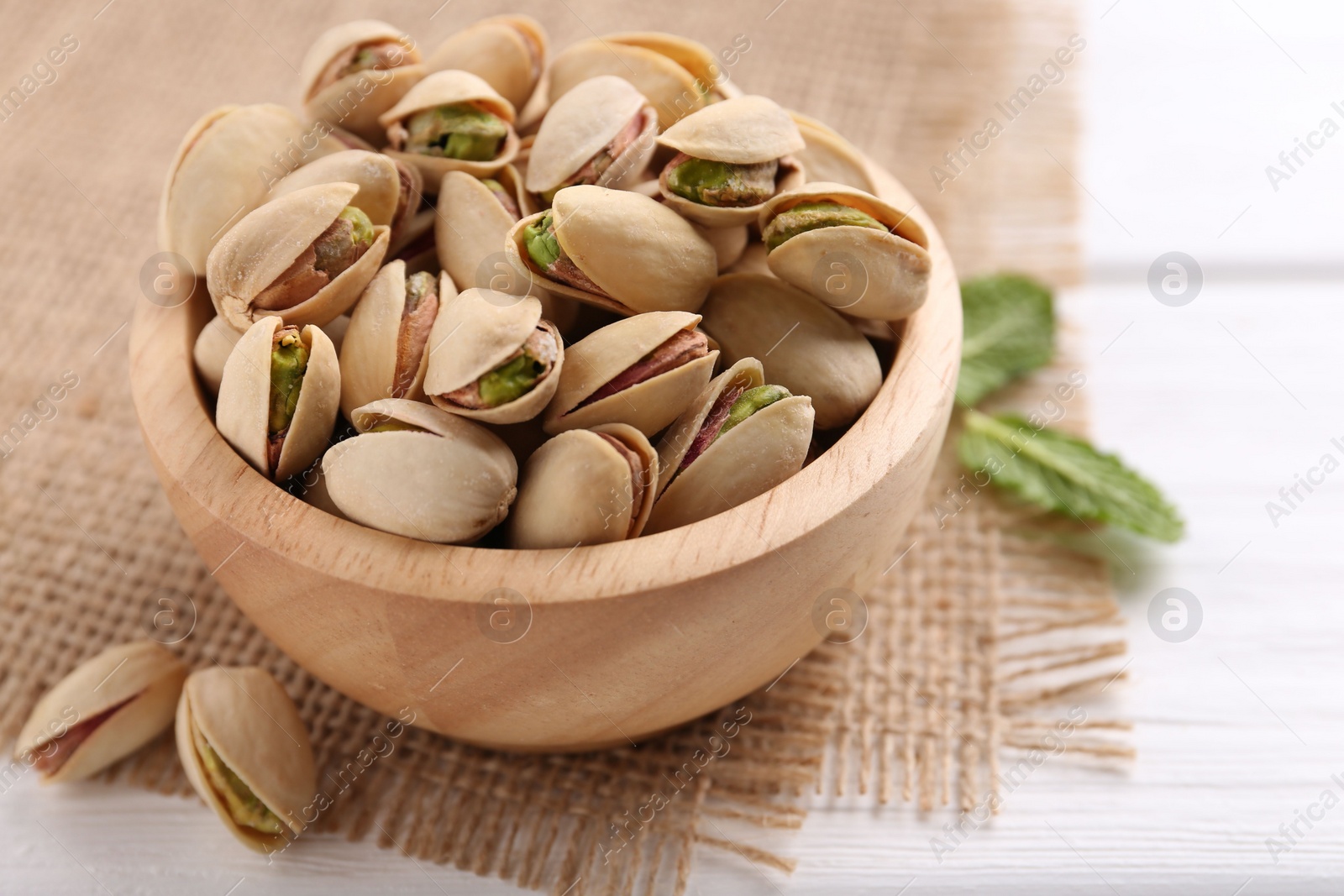 Photo of Tasty pistachios in bowl on white wooden table, closeup