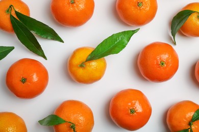 Delicious tangerines and green leaves on white background, flat lay