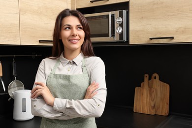 Young woman wearing green apron in kitchen, space for text