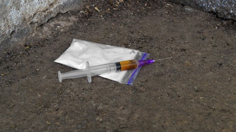 Plastic bag with powder and syringe on asphalt outdoors. Hard drugs