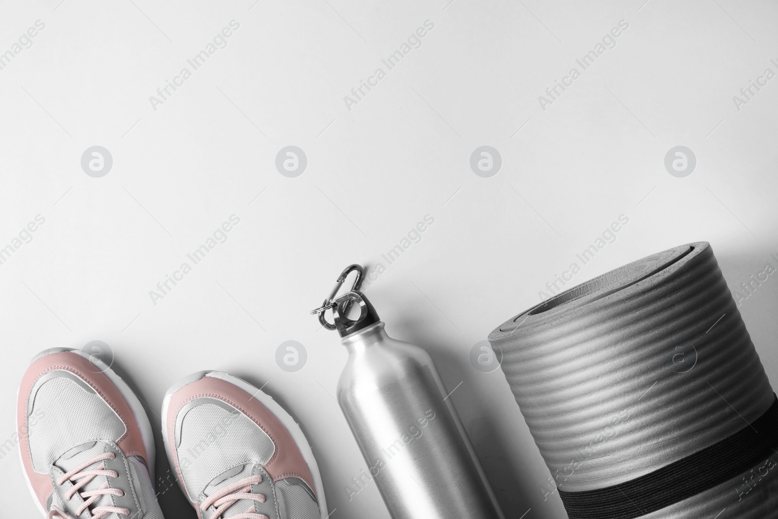 Photo of Yoga mat, sneakers and bottle of water on light background, top view with space for text. Fitness gym equipment