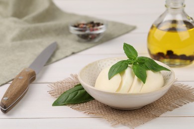 Photo of Tasty mozzarella slices, basil leaves and knife on white wooden table. Space for text