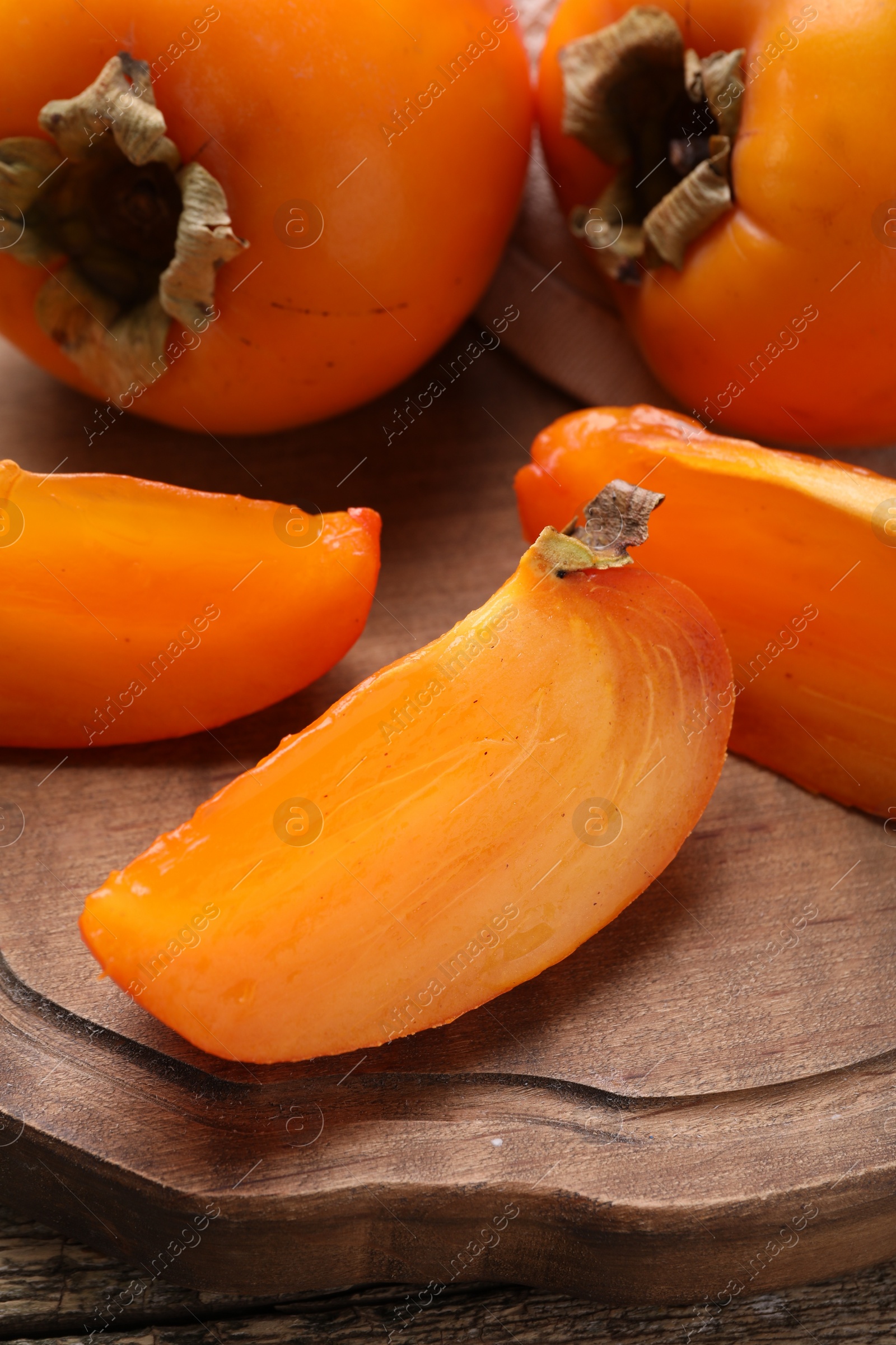 Photo of Whole and cut delicious ripe persimmons on wooden table, closeup