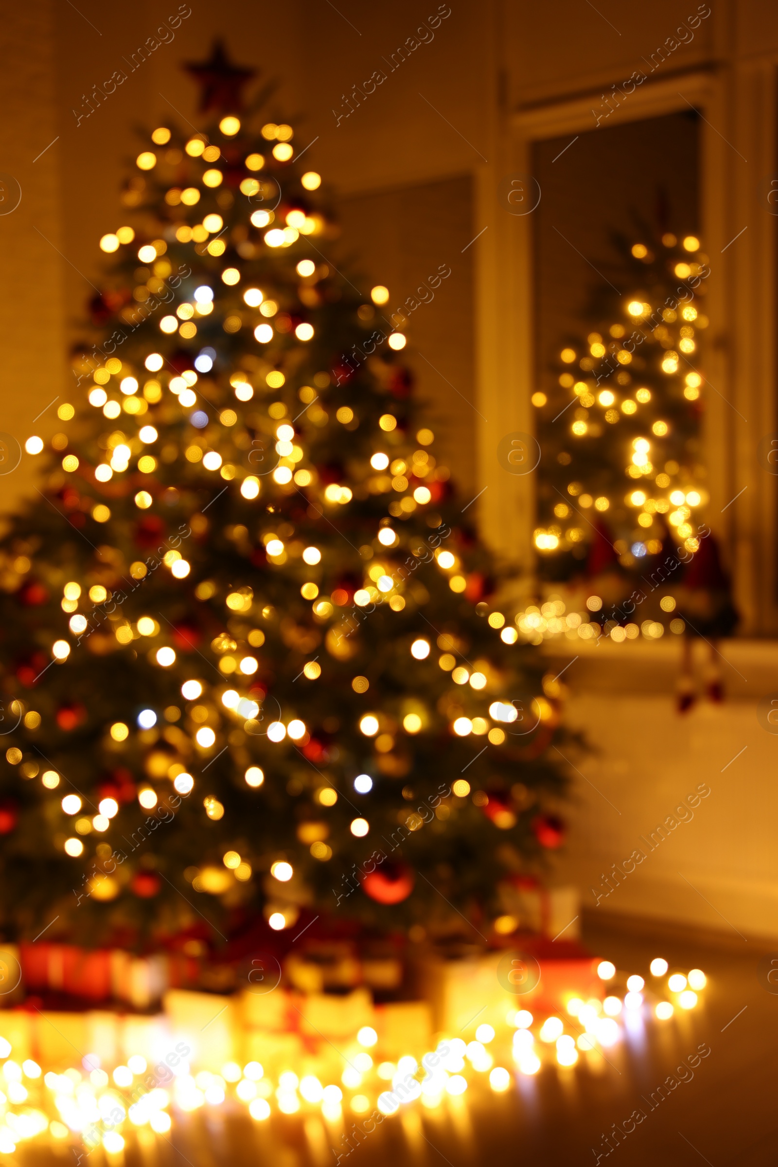 Photo of Beautiful Christmas tree, gifts and festive lights near window in room, blurred view