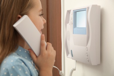 Photo of Cute little girl answering intercom call indoors, closeup