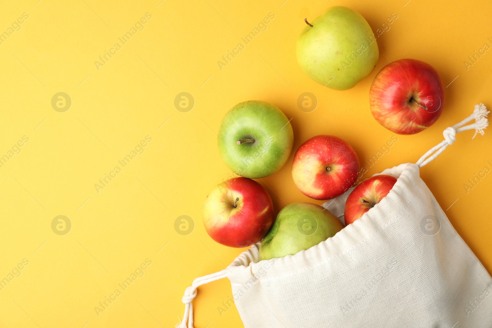 Photo of Cotton eco bag and apples on yellow background, flat lay. Space for text