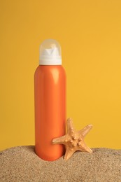 Photo of Sand with bottle of sunscreen and starfish against orange background. Sun protection