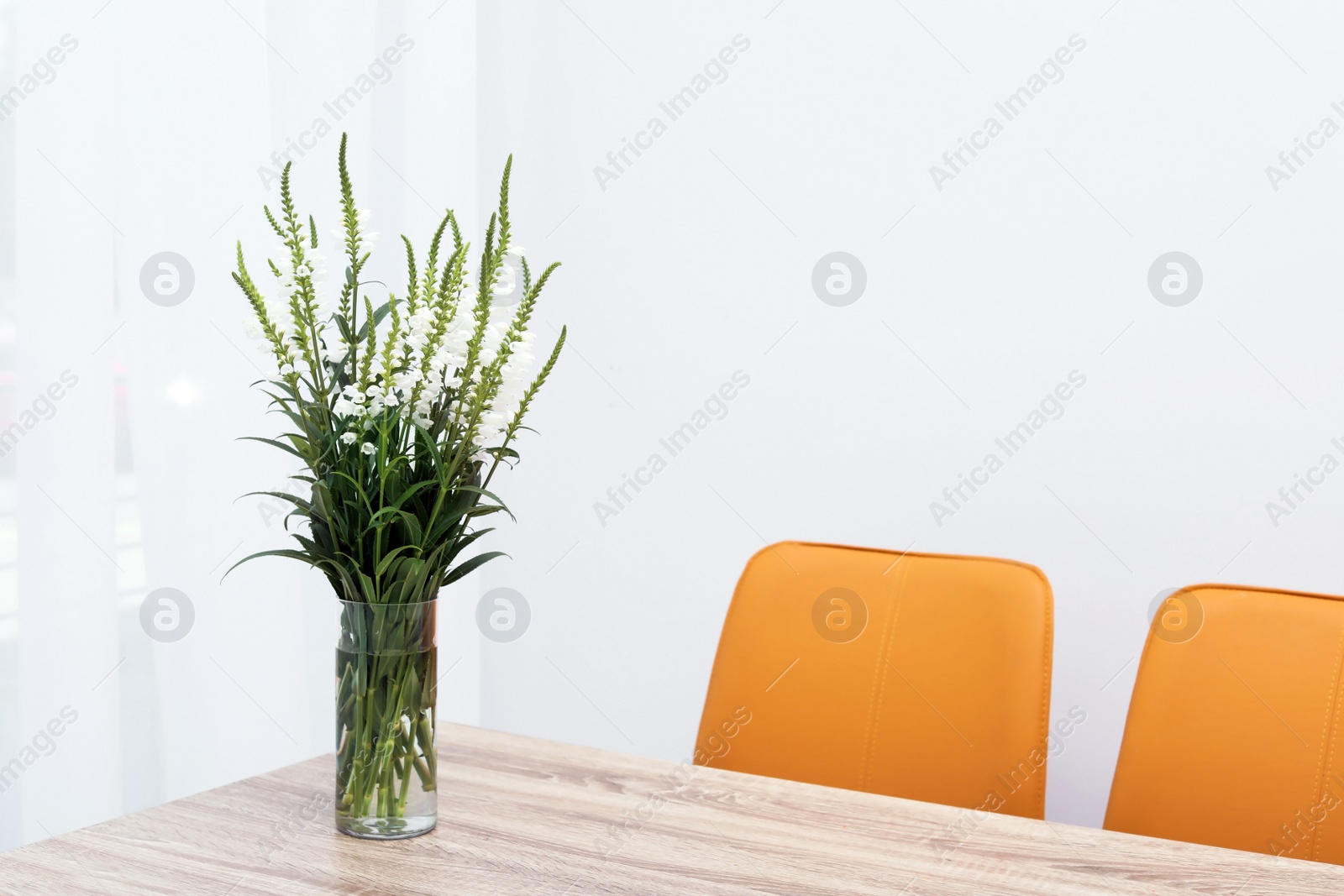 Photo of Beautiful bouquet in vase on wooden table against color background. Stylish interior