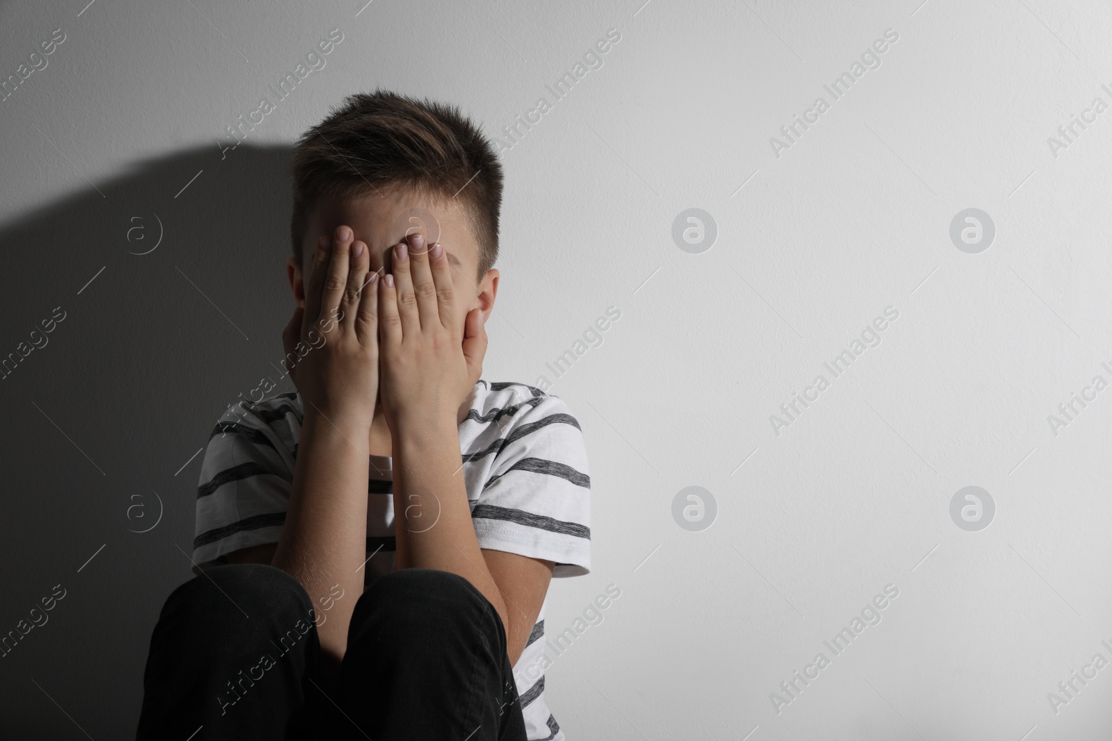 Photo of Scared little boy closing his eyes near white wall, space for text. Domestic violence concept