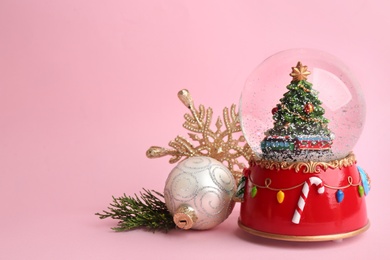 Photo of Beautiful snow globe and Christmas decor on pink background, space for text