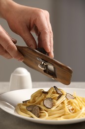 Photo of Woman slicing truffle onto fettuccine at table, closeup