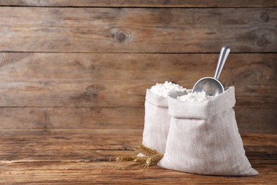 Photo of Sacks with flour and wheat spikes on wooden background. Space for text