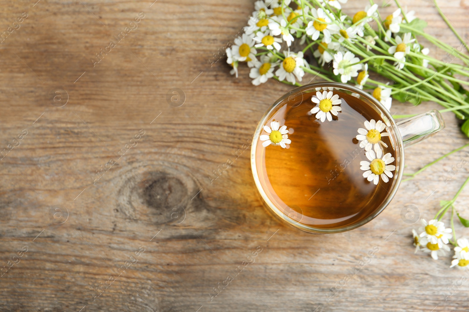 Photo of Cup of tea and chamomile flowers on wooden table, flat lay. Space for text