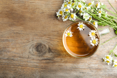 Photo of Cup of tea and chamomile flowers on wooden table, flat lay. Space for text