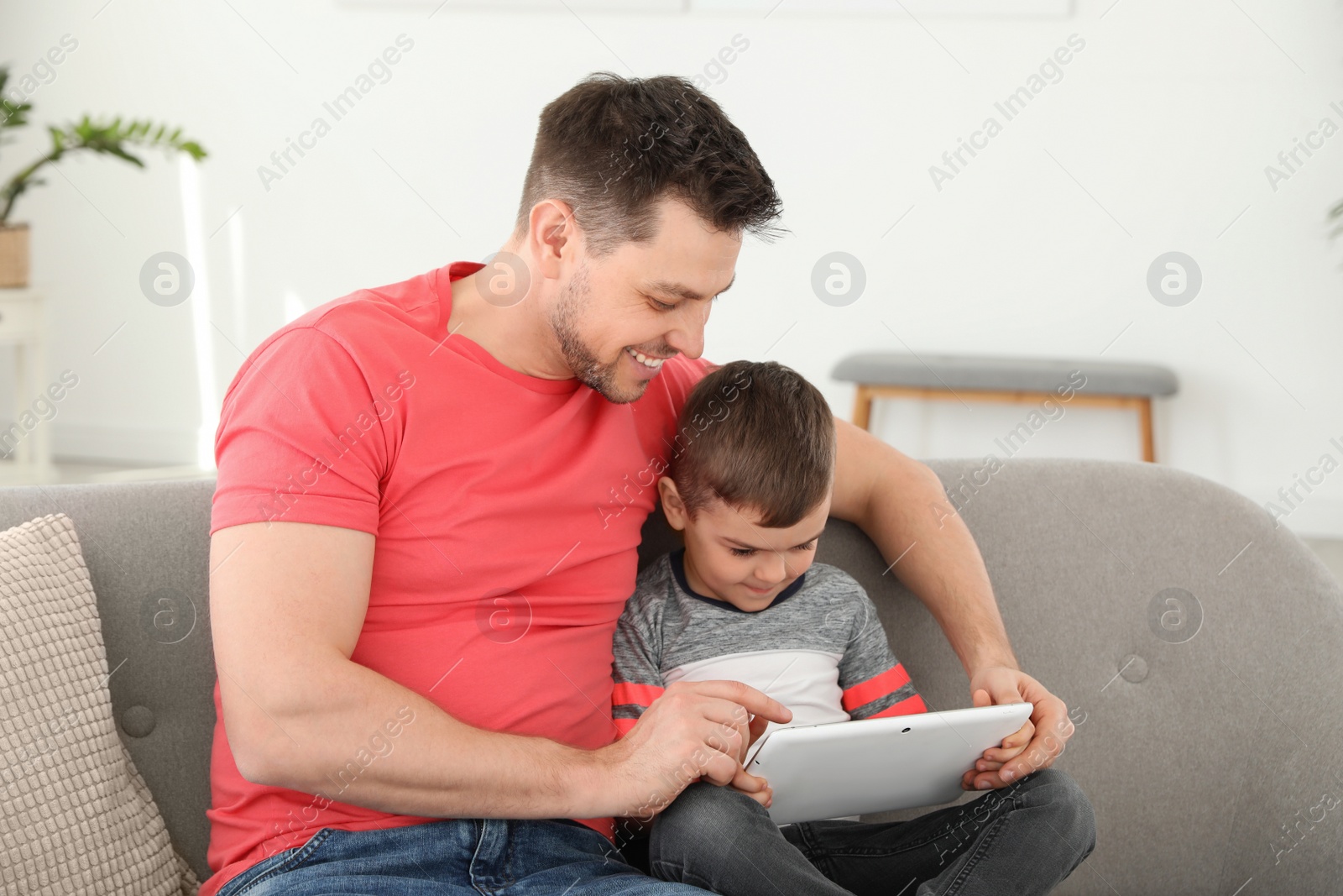 Photo of Boy and his father with tablet sitting on sofa at home. Family time