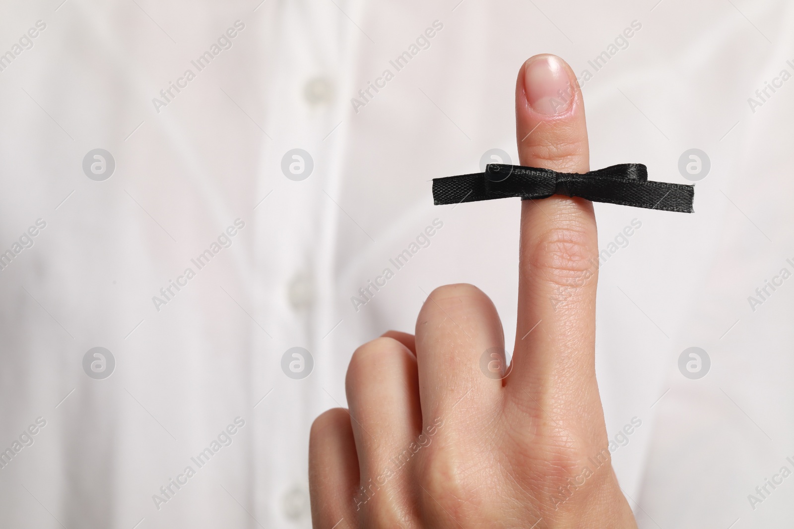 Photo of Woman showing index finger with tied black bow as reminder, closeup