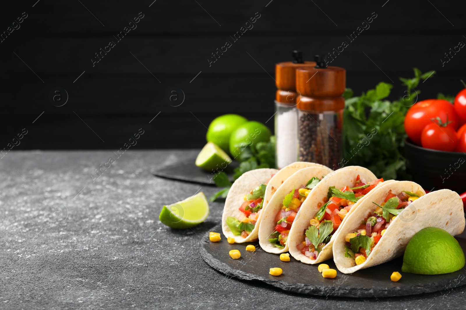 Photo of Tasty tacos with vegetables on black textured table, space for text