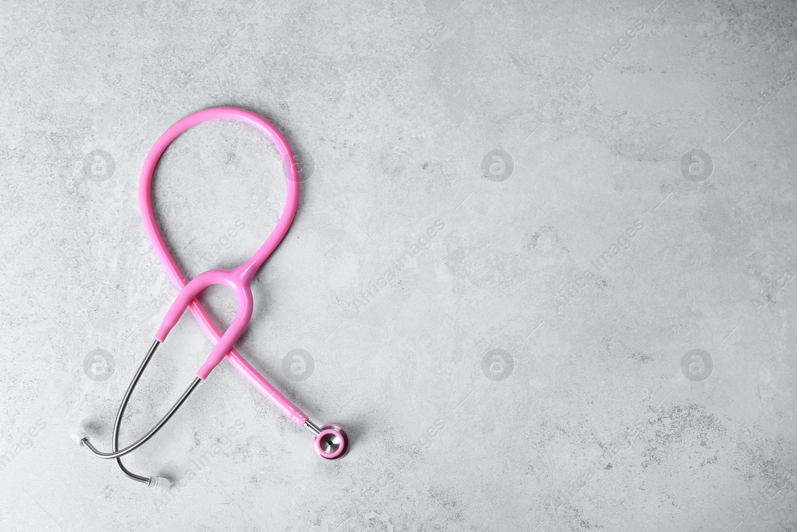 Photo of Pink stethoscope as awareness ribbon on light background, top view with space for text. Breast cancer concept