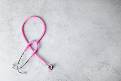 Photo of Pink stethoscope as awareness ribbon on light background, top view with space for text. Breast cancer concept