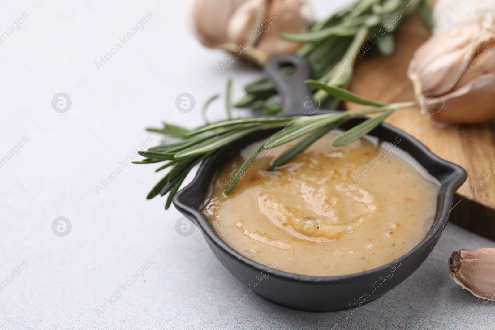 Photo of Delicious turkey gravy, rosemary and garlic on light grey table, closeup. Space for text