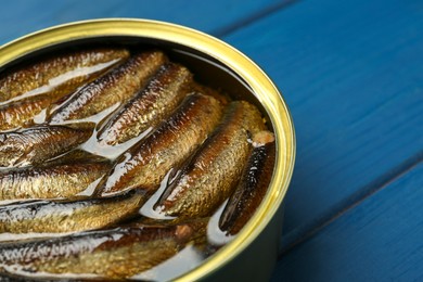 Open tin can of sprats on blue wooden table, closeup