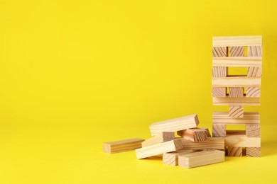 Photo of Jenga tower and wooden blocks on yellow background, space for text