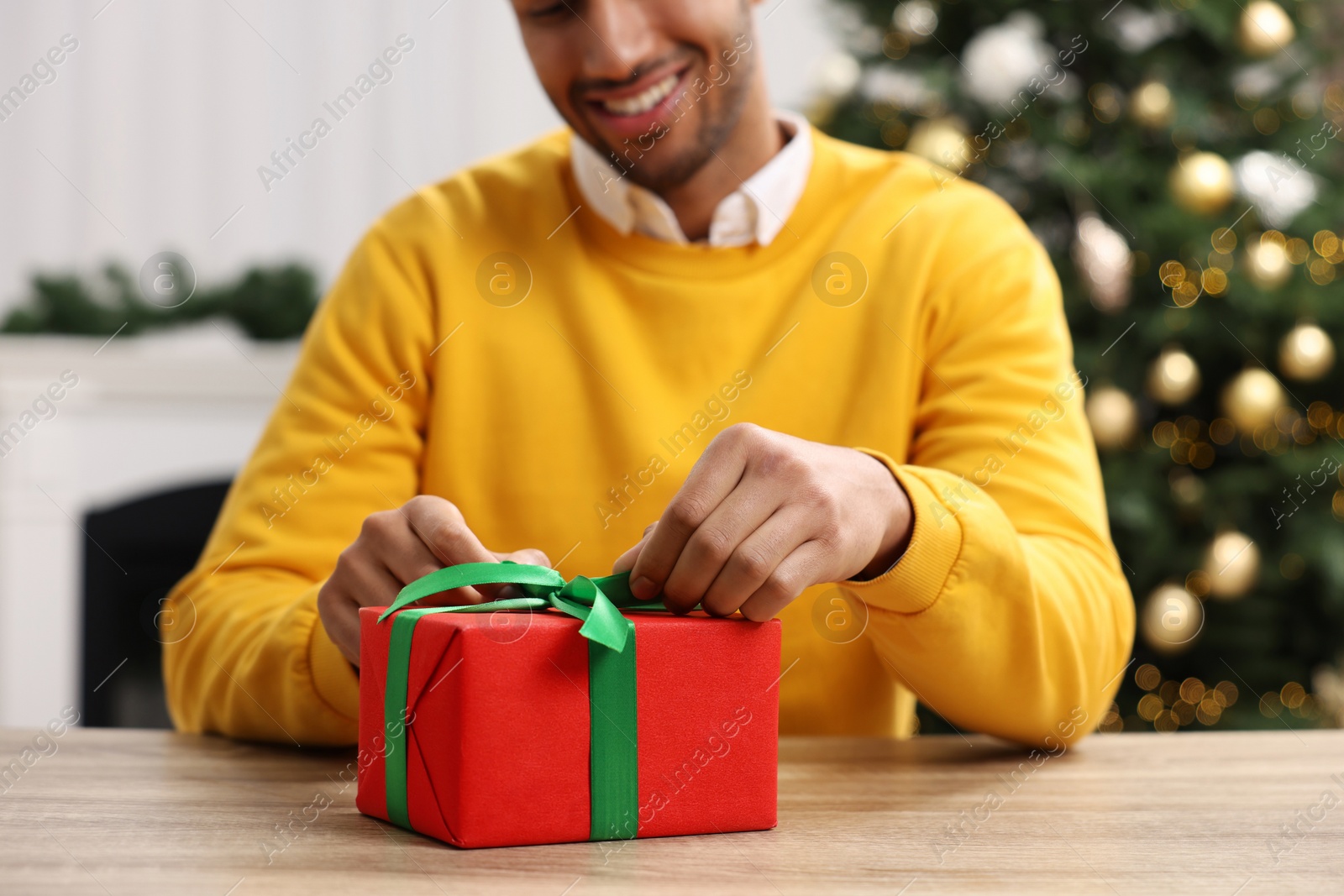 Photo of Man opening Christmas gift at wooden table in room, closeup