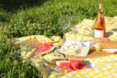 Photo of Picnic blanket with delicious food and wine on green grass outdoors