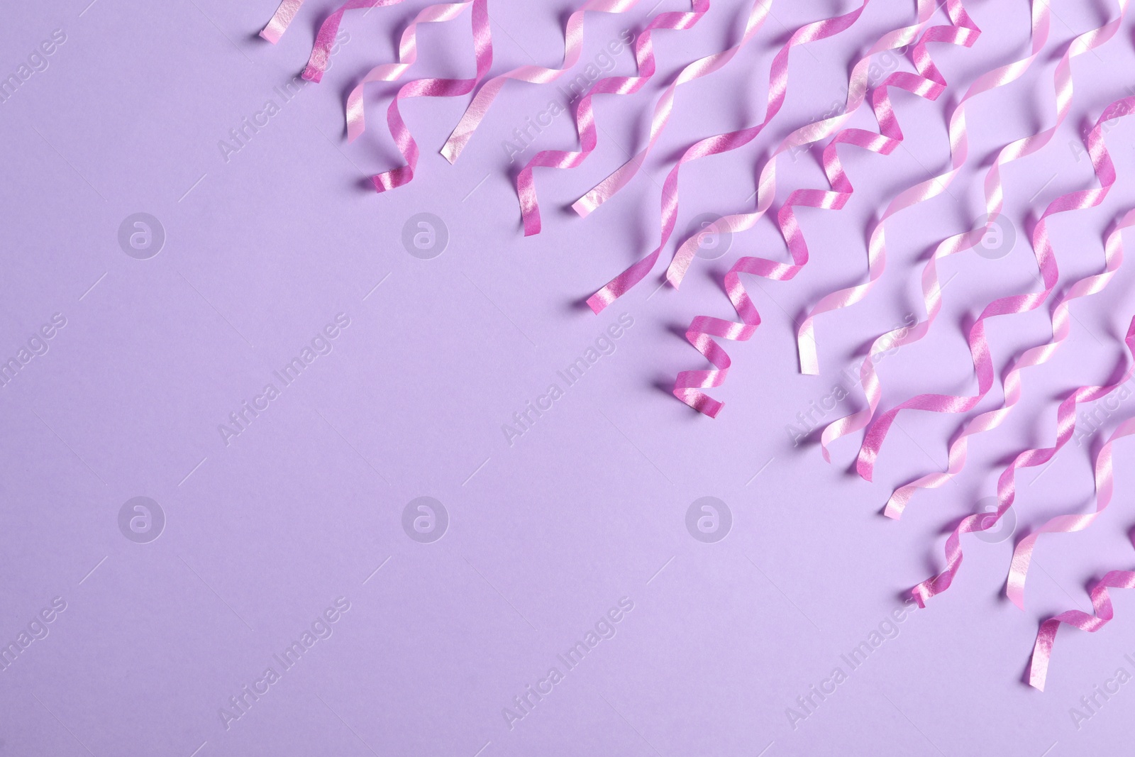 Photo of Pink serpentine streamers on light violet background, flat lay. Space for text