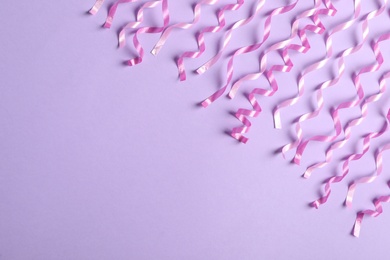 Pink serpentine streamers on light violet background, flat lay. Space for text