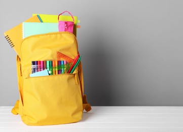 Photo of Yellow backpack with different school stationery on white table against grey background, space for text