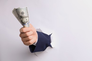Photo of Businessman breaking through white paper with money in fist, closeup. Space for text
