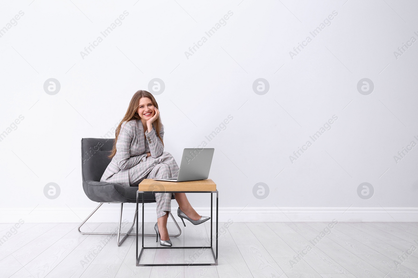 Photo of Young woman working with laptop in armchair indoors. Space for text