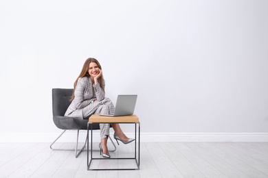 Young woman working with laptop in armchair indoors. Space for text