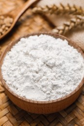 Photo of Wheat flour in wooden bowl on wicker mat, closeup