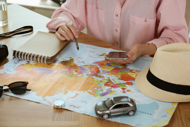 Photo of Woman with world map and smartphone planning trip at wooden table, closeup