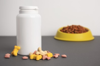 Bottle with vitamins and dry pet food in bowl on grey table, closeup. Space for text