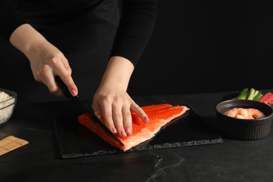 Chef cutting salmon for sushi at dark textured table, closeup