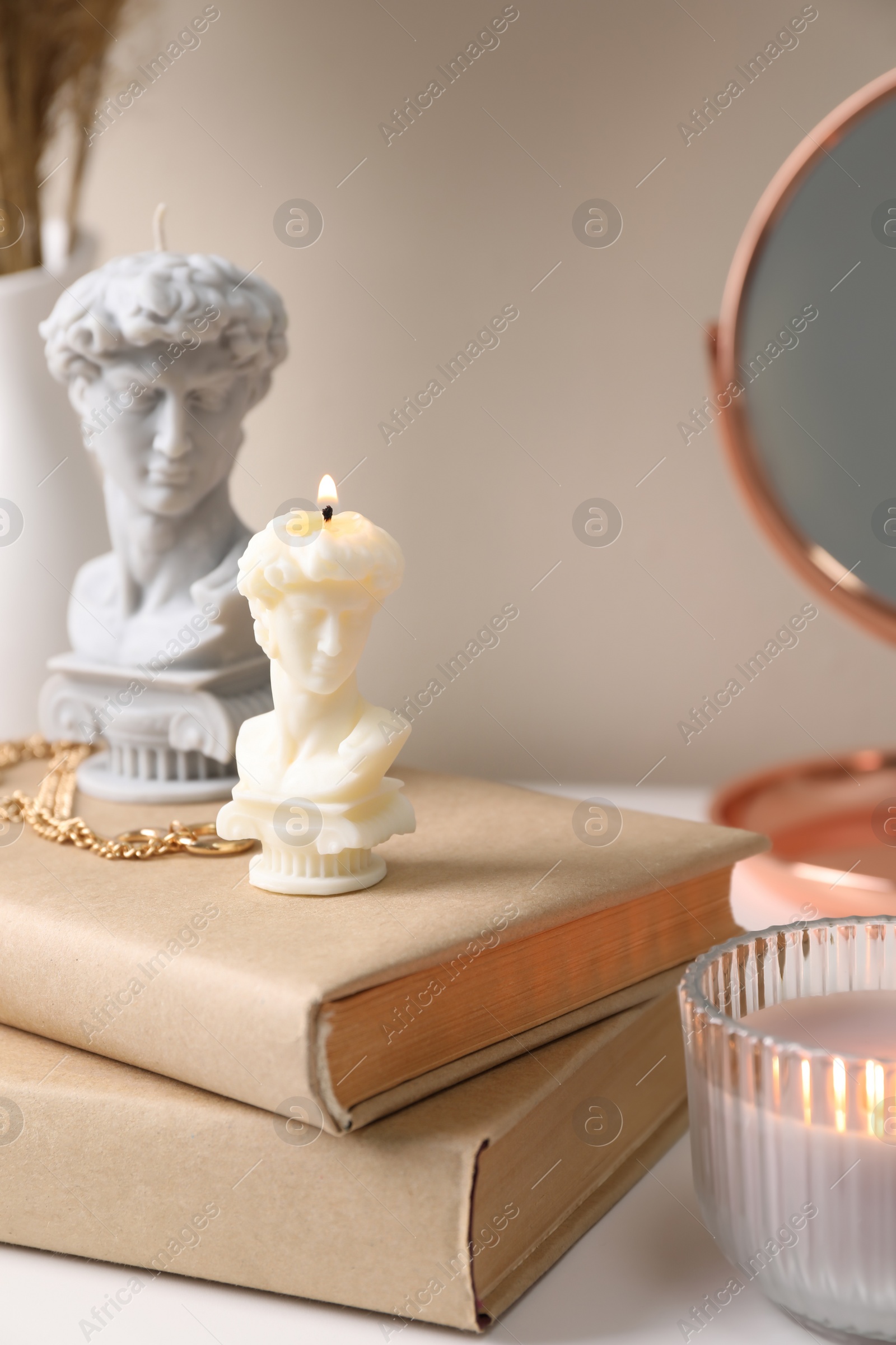 Photo of Beautiful David bust candles and books on table