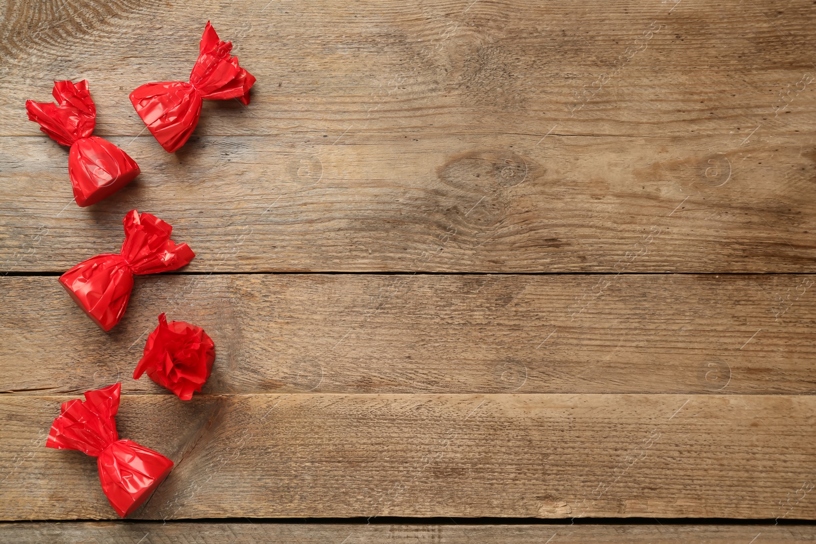 Photo of Candies in red wrappers on wooden table, flat lay. Space for text