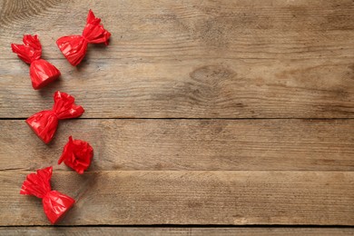 Candies in red wrappers on wooden table, flat lay. Space for text