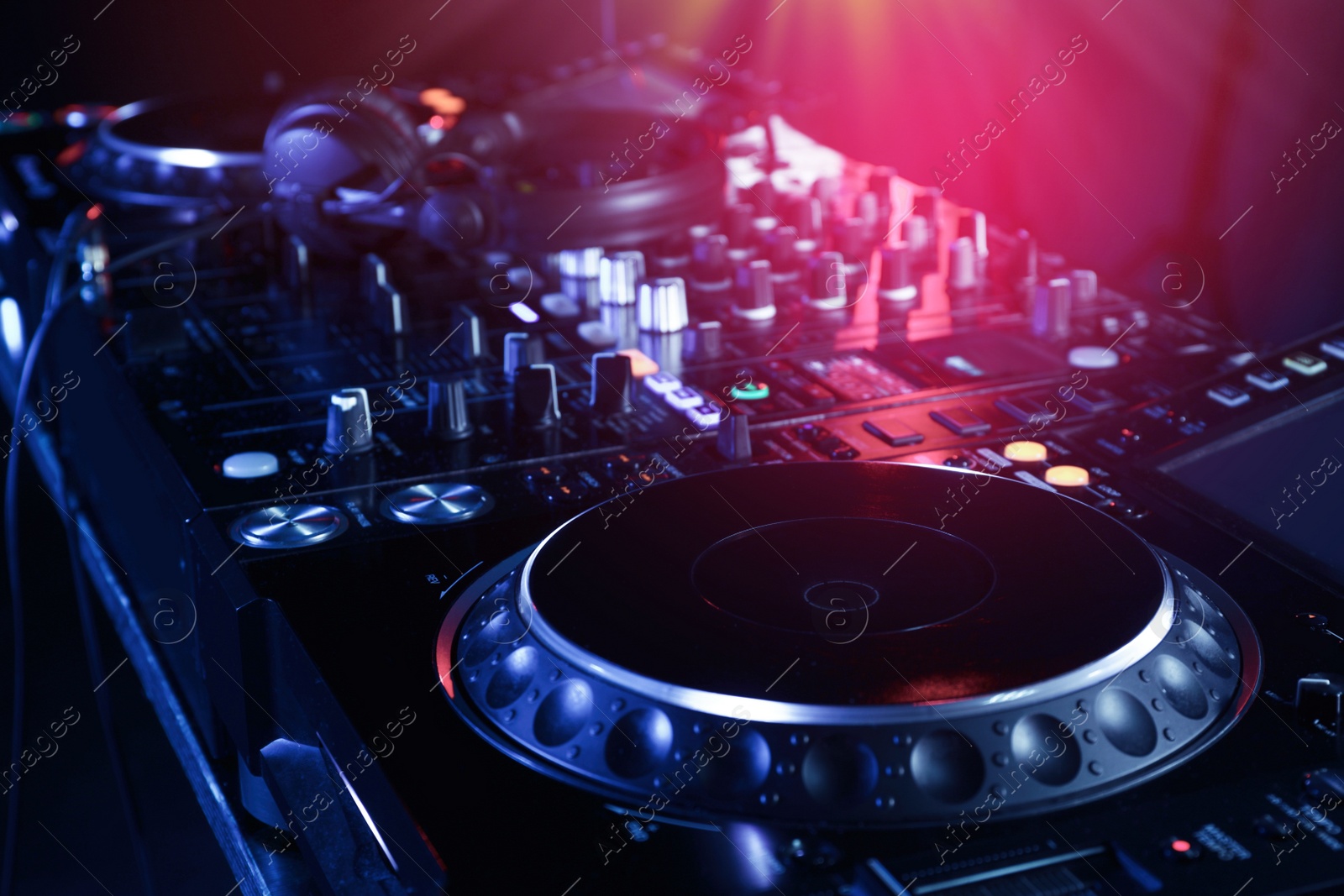 Photo of Closeup view of modern DJ controller with headphones on color background