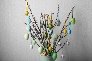 Photo of Beautiful willow branches with painted eggs on light grey background, closeup. Easter decor