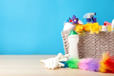 Photo of Wicker basket with spring flowers and cleaning supplies on wooden table. Space for text
