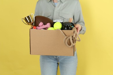 Photo of Woman holding box of unwanted stuff on yellow background, closeup