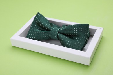 Photo of Stylish color bow tie with polka dot pattern in box on light green background